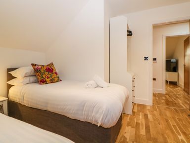 A bedroom with two beds one with a floral pillow and rolled towels a white wardrobe and wooden flooring at Riviera Heights Paignton