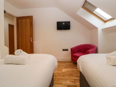 A bedroom with two beds with white linens a wall mounted tv a pink chair a skylight window and wooden doors at Riviera Heights in Paignton