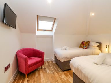 A bedroom with two single beds a red armchair a wall-mounted television and a skylight window at Riviera Heights in Paignton