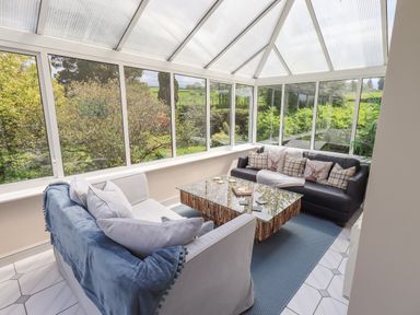 A conservatory with two sofas a glass coffee table and large windows overlooking greenery at Greenstyles in Bowness-On-Windermere