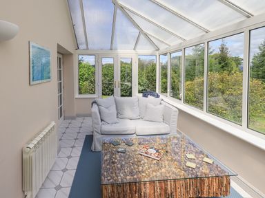 A sunroom with a white sofa and a glass coffee table with corks and wooden base at Greenstyles in Bowness-On-Windermere