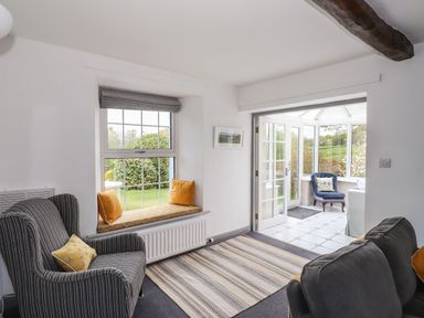 A sitting room with striped armchair cushions window seat and doorway leading to a conservatory at Greenstyles in Bowness-On-Windermere