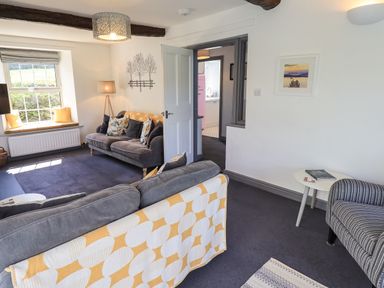 A living room with grey sofas cushions and a window seat beside a doorway leading to a kitchen at Greenstyles in Bowness-On-Windermere