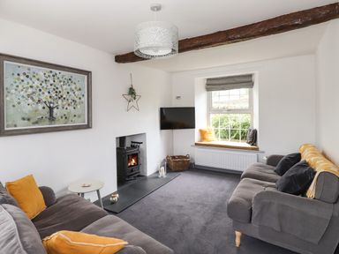 A living room with grey sofas yellow cushions a wood stove and window seat at Greenstyles in Bowness-On-Windermere
