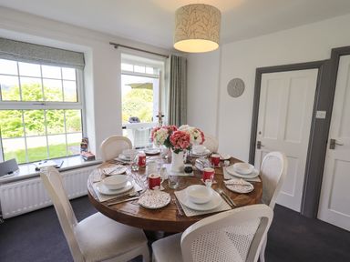 A dining room with a round wooden table set for six and a door leading outside at Greenstyles in Bowness-On-Windermere