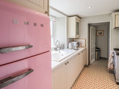 A kitchen with a pink SMEG fridge white cabinets a sink a microwave and a patterned floor at Greenstyles in Bowness-On-Windermere