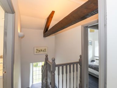 A staircase landing with a wooden railing exposed ceiling beam and doors leading to a bedroom and bathroom at Greenstyles in Bowness-On-Windermere