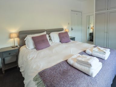 A bedroom with a double bed with white linens purple cushions and folded towels on a purple blanket at Greenstyles in Bowness-On-Windermere