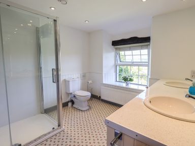 A bathroom with a shower cubicle toilet double sink and a window with a plant on the sill at Greenstyles in Bowness-On-Windermere