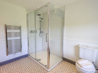 A bathroom with a glass shower enclosure a toilet with folded towels and a chrome towel radiator at Greenstyles in Bowness-On-Windermere