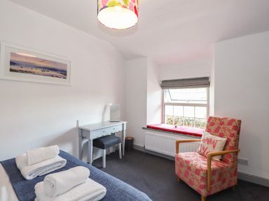 A bedroom with a bed with towels a dressing table and a floral armchair near a window at Greenstyles in Bowness-On-Windermere