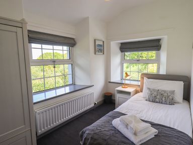 A bedroom with a single bed side table and two windows at Greenstyles in Bowness-On-Windermere