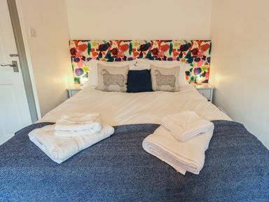 A bedroom with a bed featuring a colorful headboard two sheep pillows and towels on a blue blanket at Greenstyles in Bowness-On-Windermere