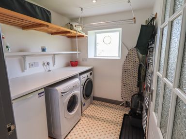A laundry room with a washing machine dryer ironing board and shelves at Greenstyles in Bowness-On-Windermere