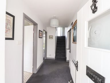 A hallway with grey carpet leading to a staircase with doorways on the sides and framed pictures on the walls at Greenstyles in Bowness-On-Windermere