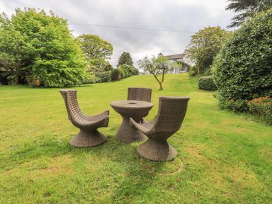 A garden with three wicker chairs and a round wicker table on grass at Greenstyles in Bowness-On-Windermere