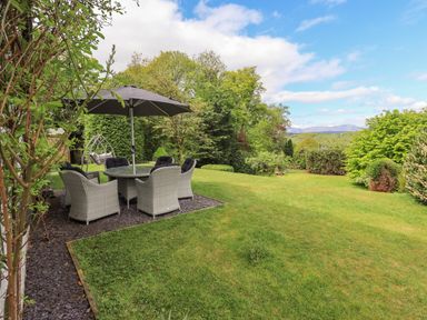 An outdoor patio area with a round table and six chairs under a large umbrella in a garden at Greenstyles in Bowness-On-Windermere