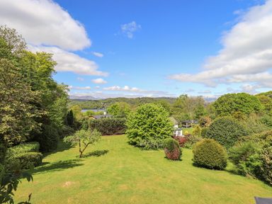 A large garden with various trees and bushes and a view of a lake at Greenstyles in Bowness-On-Windermere
