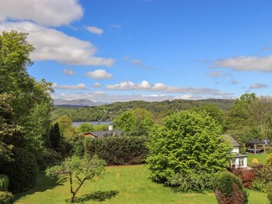 A garden with trees and grass overlooking a lake and hills at Greenstyles in Bowness-On-Windermere