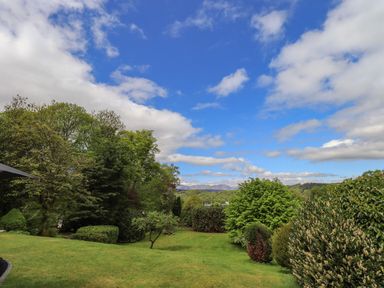 A garden with grass and various trees under a blue sky at Greenstyles in Bowness-On-Windermere