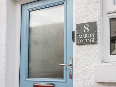 A blue front door with frosted glass and a house sign reading 8 Marlin Cottage in Conwy