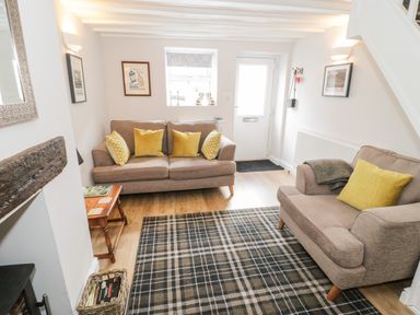 A living room with two beige sofas and yellow cushions a checkered rug a wooden side table and wall art at Marlin Cottage in Conwy