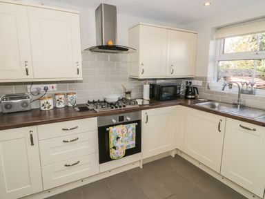 A kitchen with cream cabinets a gas stove a microwave a toaster and a sink with a window at Marlin Cottage Conwy