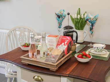 A dining table set with tea cups strawberries a French press flowers and snacks at Marlin Cottage in Conwy