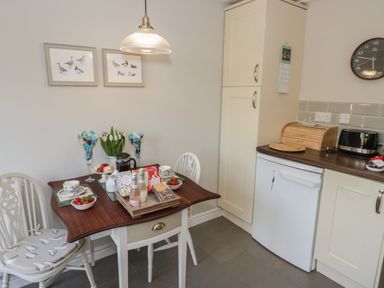 A kitchen corner with a small wooden table set for tea and two white chairs at Marlin Cottage in Conwy