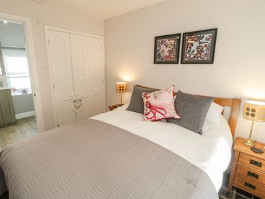 A bedroom with a bed with pillows and blanket two framed pictures on the wall two bedside tables with lamps and a closet with double doors at Marlin Cottage in Conwy