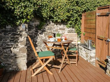 A small outdoor patio with a wooden table and two chairs next to a stone wall covered in ivy with a wooden fence at Marlin Cottage in Conwy
