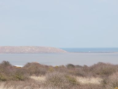 A view of bushes and grass with a body of water and a hill in the background at Buck Place The Bay Filey