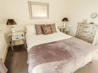 A bedroom with a double bed pillows bedside tables lamps a chest of drawers and a wall mirror at Buck Place The Bay - Filey