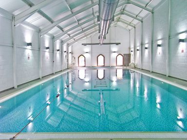 An indoor swimming pool with blue water inside a white wall structure at Buck Place in The Bay Filey