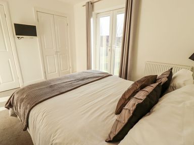 A bedroom with a bed with pillows a gray blanket a wall-mounted television French doors and a double closet at Buck Place The Bay Filey