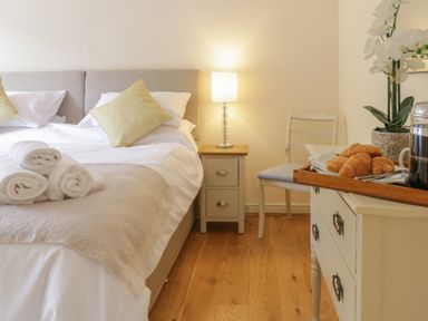 A bedroom with a bed with pillows and towels beside a nightstand with a lamp and a chair next to a dresser with croissants and a coffee press at Hendre in Penybontfawr