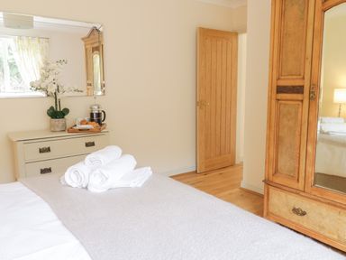 A bedroom with a bed holding folded towels a wooden wardrobe with a mirror a dresser with a tray of coffee and pastries and a mirror above it at Hendre in Penybontfawr
