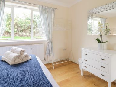 A bedroom with a bed with folded towels on a blue blanket a white chest of drawers with a potted plant a mirror and a window with curtains at Hendre in Penybontfawr