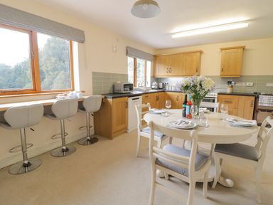A kitchen with a dining table set for four and three bar stools by the window at Hendre in Penybontfawr