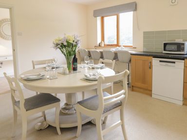 A dining area with a round table set for four and a vase of flowers by a window with bar stools in a kitchen at Hendre in Penybontfawr