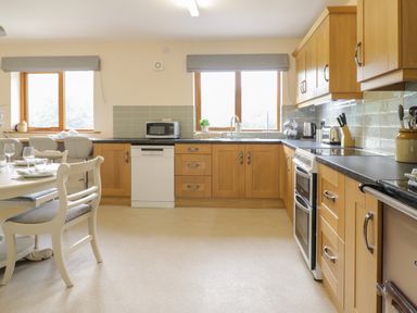 A kitchen with wooden cabinets a dining table and chairs microwave and oven at Hendre in Penybontfawr