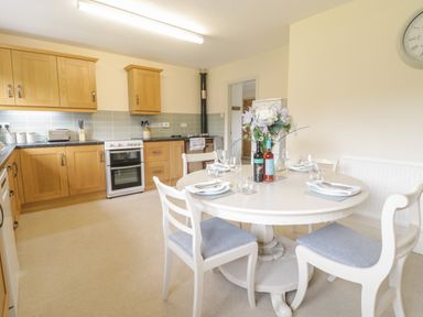 A kitchen with wooden cabinets and a dining table set with plates glasses and bottles at Hendre in Penybontfawr