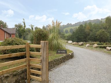 A gravel driveway leading to a house with wooden fencing and a stone sign that says Hendre at Penybontfawr