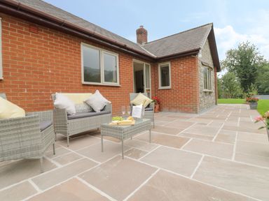 An outdoor patio with wicker furniture and a table set with wine and snacks at Hendre in Penybontfawr
