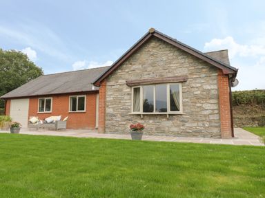 A house with stone and brick exterior with windows a garage door a patio with outdoor seating and potted plants at Hendre in Penybontfawr