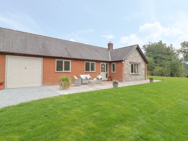 A bungalow with a garage and outdoor seating on a patio in a garden at Hendre in Penybontfawr