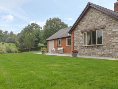 A stone and brick house with a patio and lawn with outdoor furniture and potted plants at Hendre in Penybontfawr