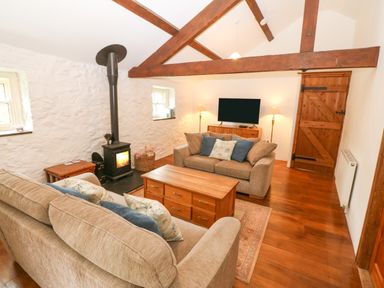 A living room with two sofas a wood stove a wooden coffee table a television and wooden beams at Nant Bach in Boduan near Nefyn