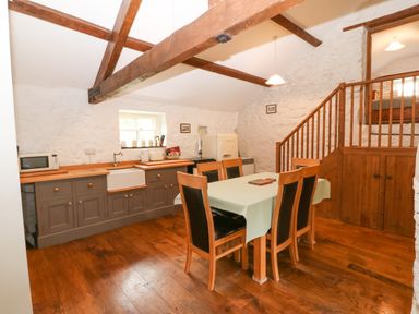 A kitchen with a dining table and chairs wooden beams on the ceiling and stairs leading to a loft at Nant Bach Boduan near Nefyn