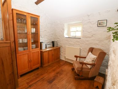 A room with a wooden cabinet holding dishes and glasses and a brown armchair next to a small window at Nant Bach in Boduan near Nefyn